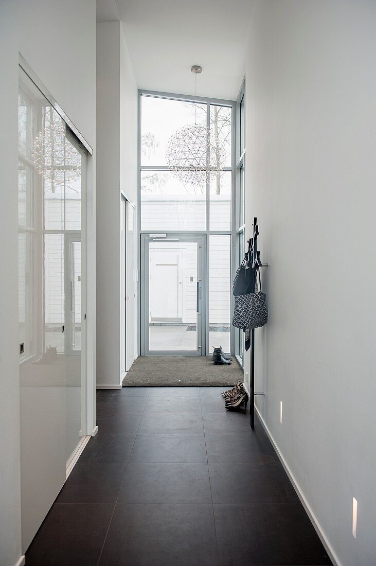 High-ceilinged narrow hallway with black-tiled floor, fitted cupboards with white sliding doors to one side and glazed house entrance at far end
