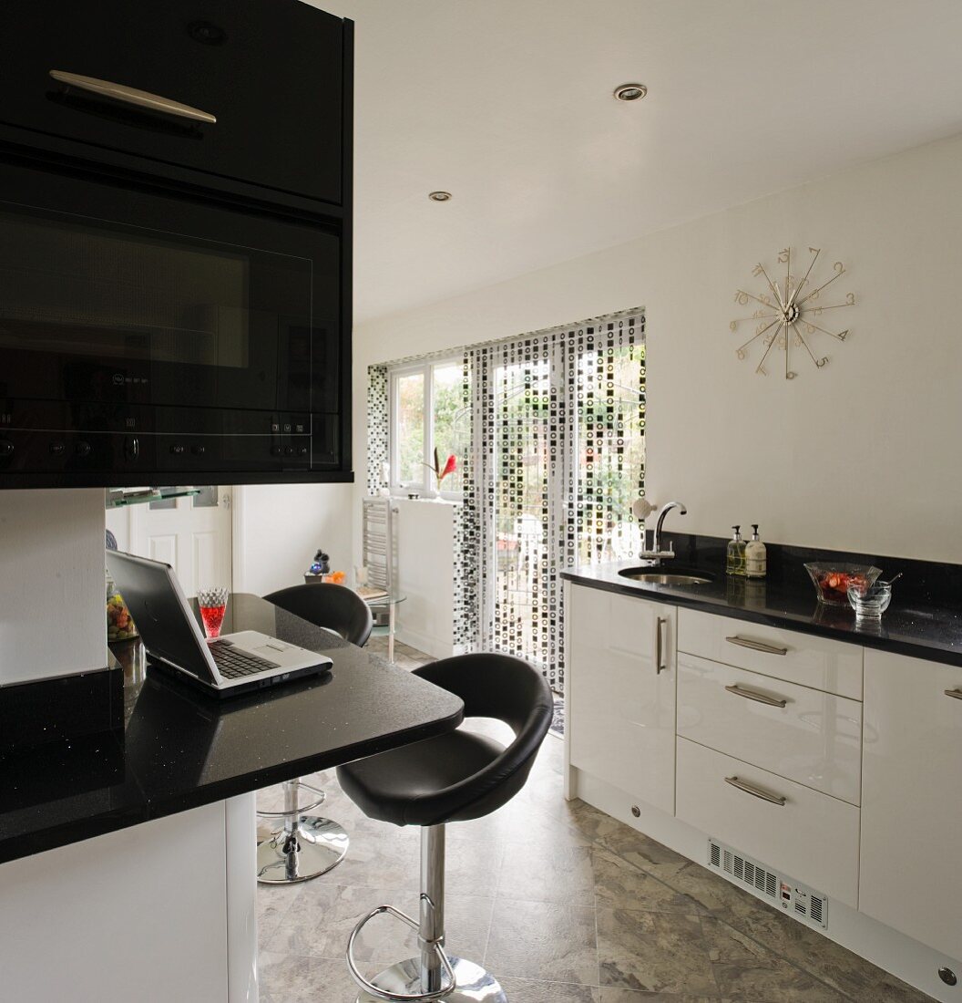 Encircling counter with black granite worksurface and glossy white fronts in black and white kitchen