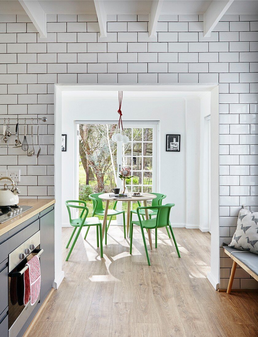 Floor-to-ceiling white wall tiles in kitchen and open doorway with view of dining area with green designer chairs