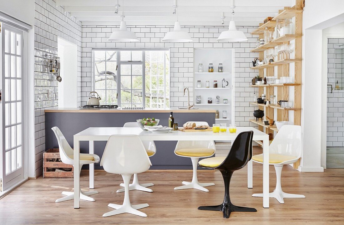 Retro Schalenstühle um weissen Tisch in offener Küche mit Theke und weiss gefliesten Wänden