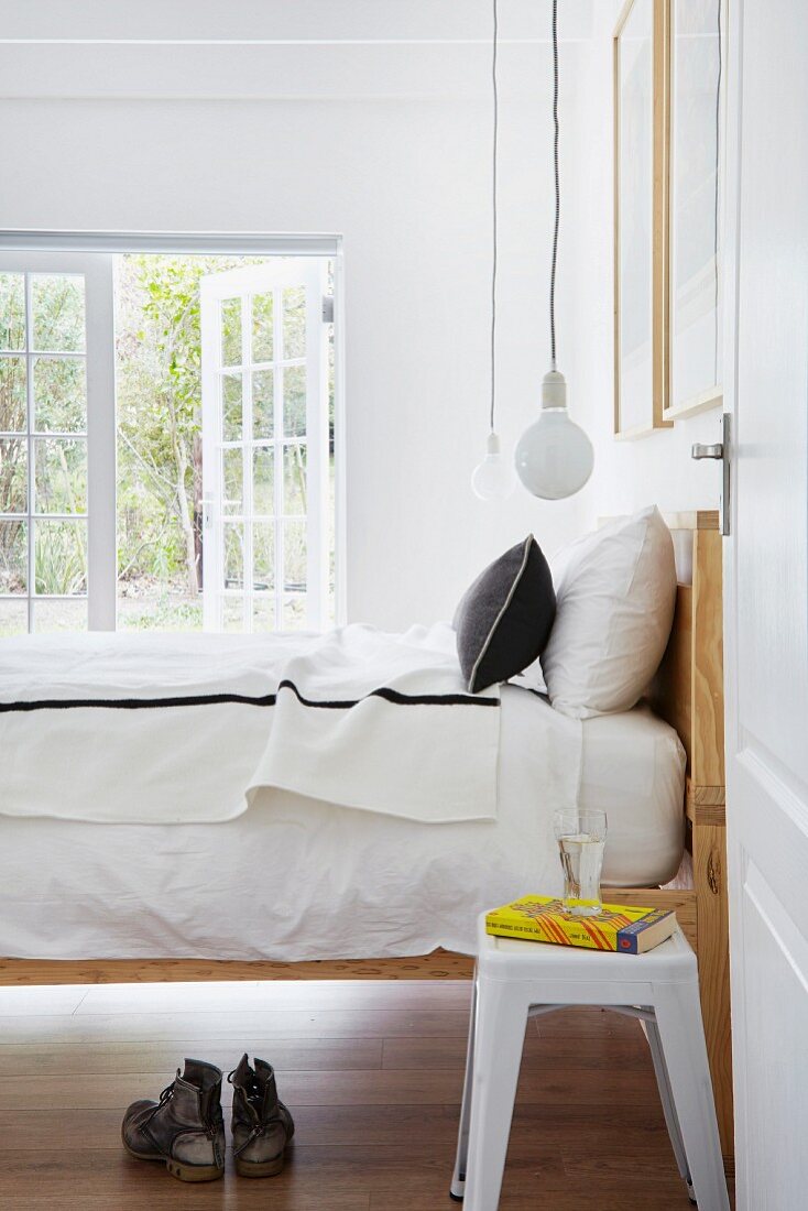 Offene Tür und Blick auf Retro Hocker neben Bett mit Holzgestell