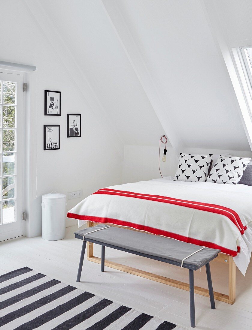 Schlichte Kleiderbank vor Doppelbett mit rot-weiss gestreifter Tagesdecke unter Dachschräge in Schlafzimmer