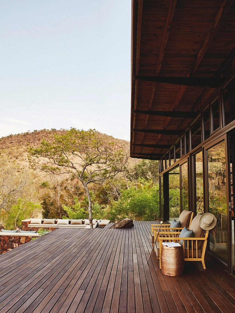 Brüstungsfreie Holzterrasse mit Armlehnsessel vor Fensterfront, im Hintergrund Safari-Landschaft