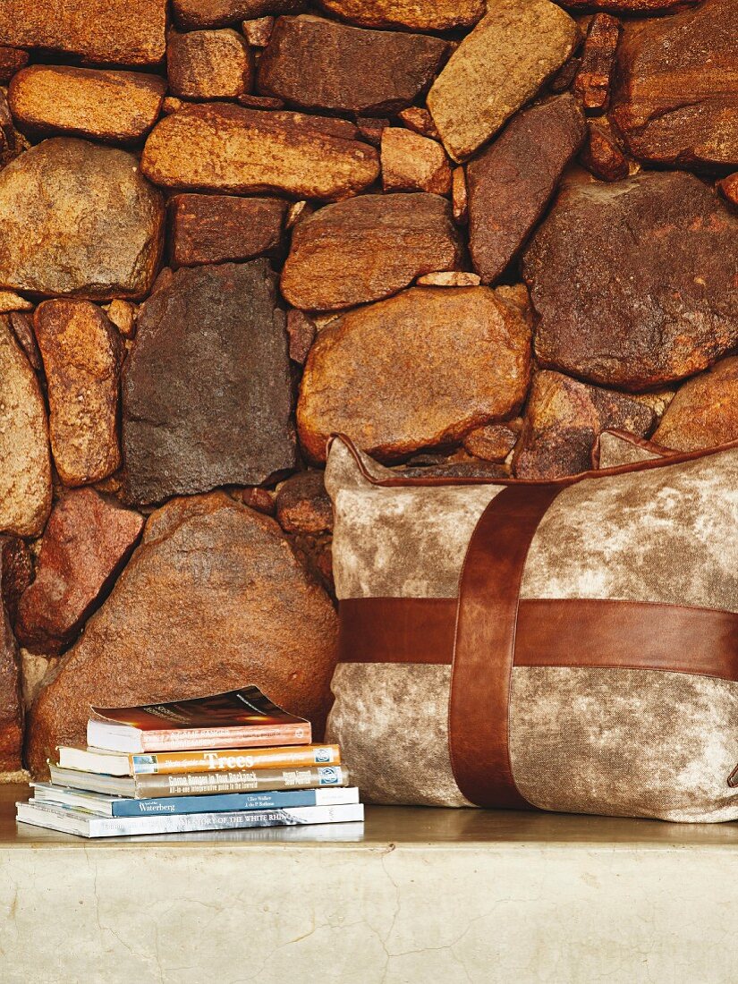 Betonsitzfläche mit Kissen und Bücherstapel vor Natursteinwand