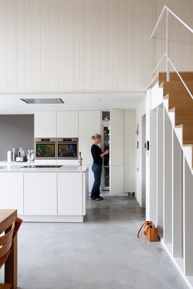 Woman in open-plan kitchen with white island counter and fitted cupboards in modern loft apartment