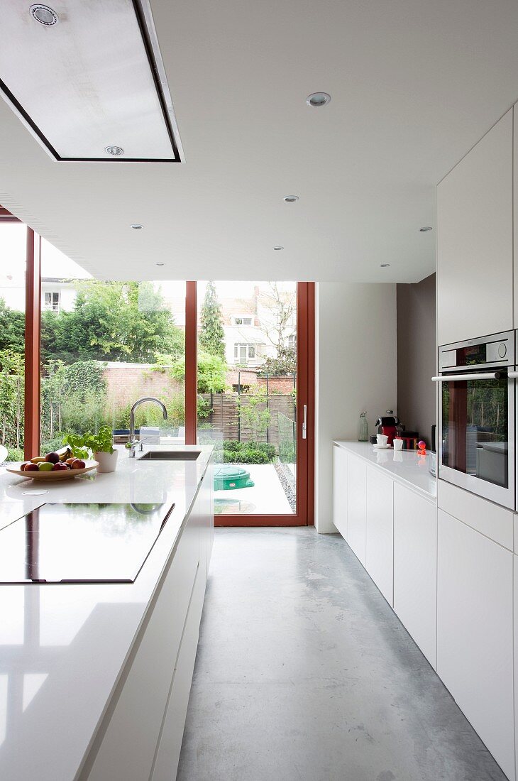Offene Küche in Weiß mit Betonboden, im Hintergrund Terrassentür