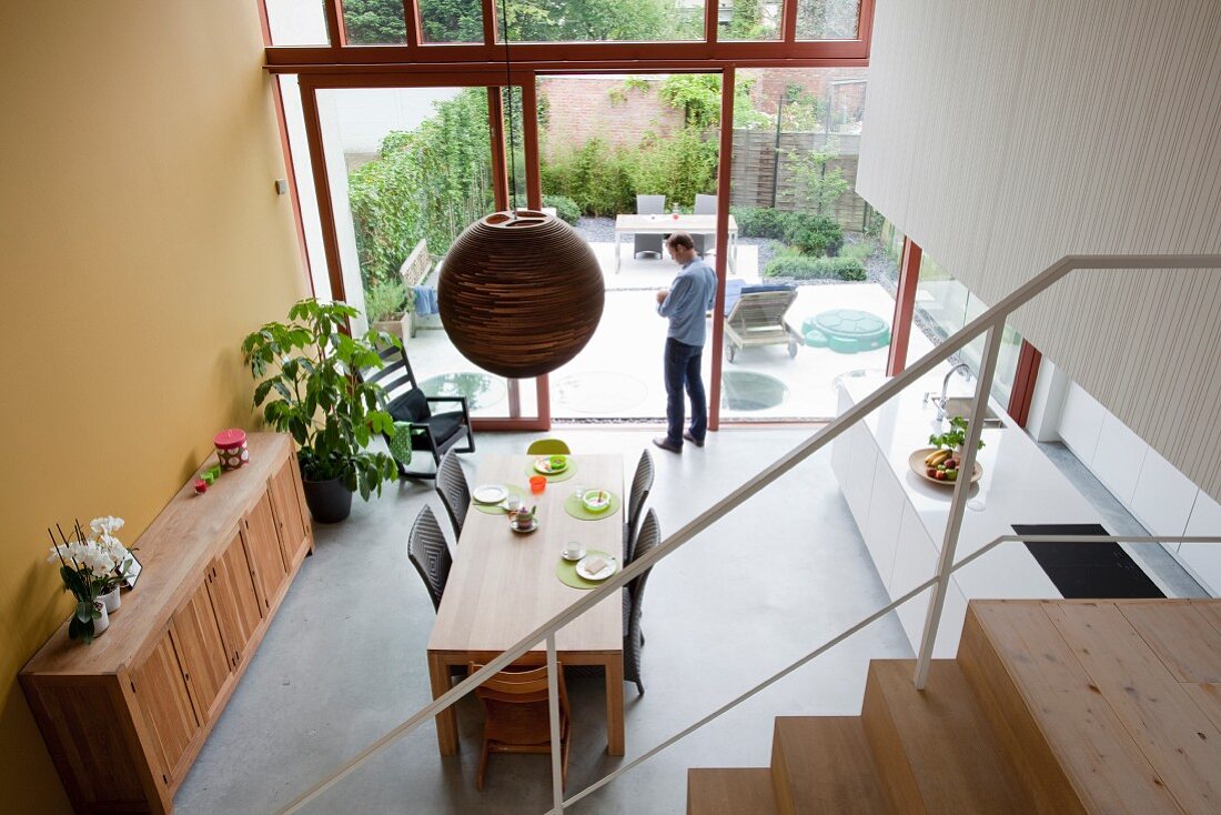 Blick von Treppe in offener Küche mit Essbereich, im Hintergrund Mann an offener Schiebetür vor Terrasse