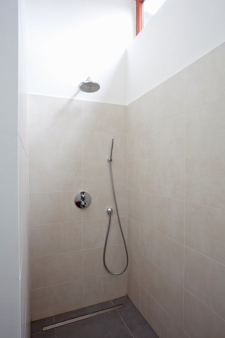 Modern shower area with contemporary tap fittings on sand-coloured wall tiles and rainfall shower head