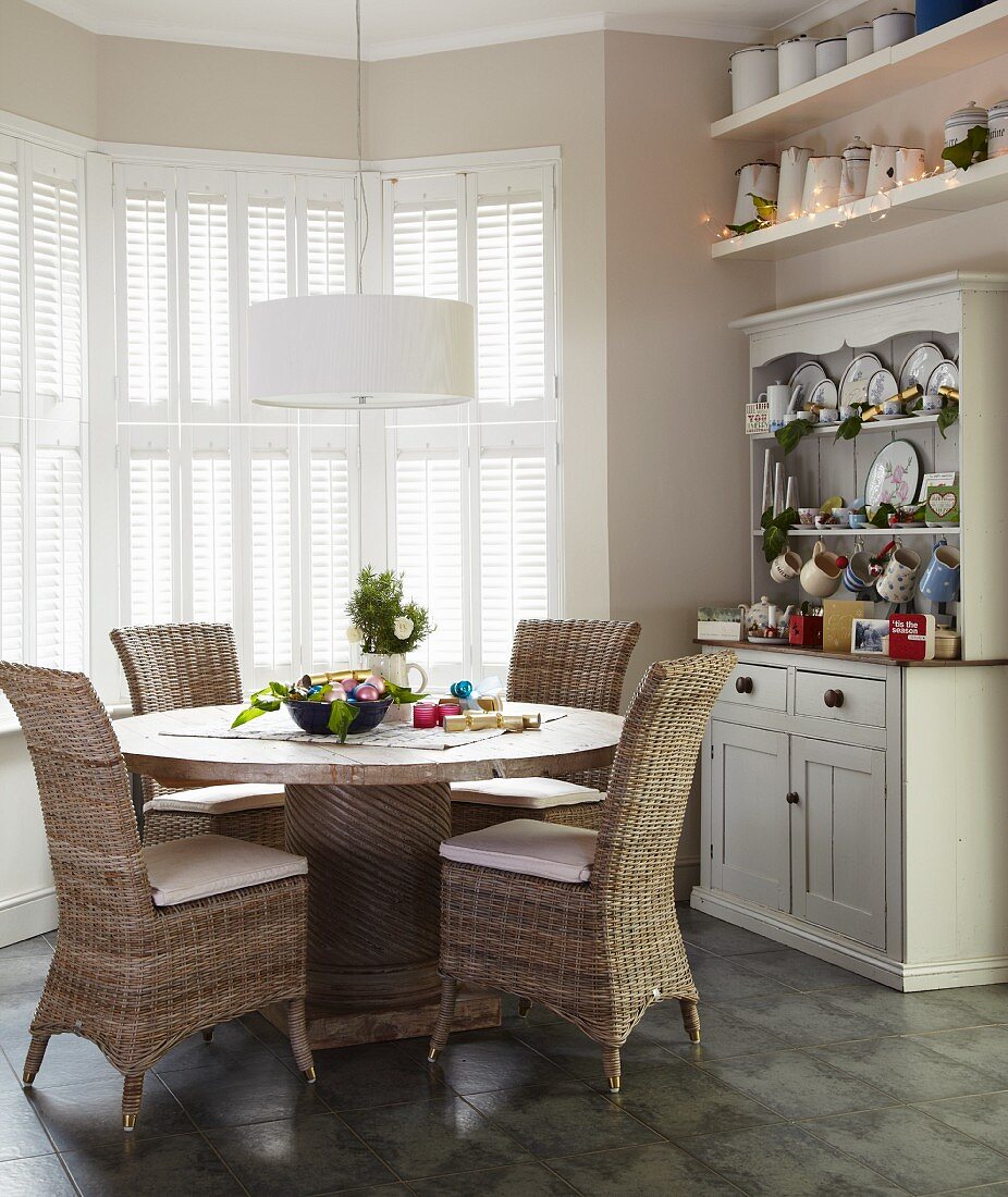 Wicker chairs at round dining table below white pendant lamp in window bay