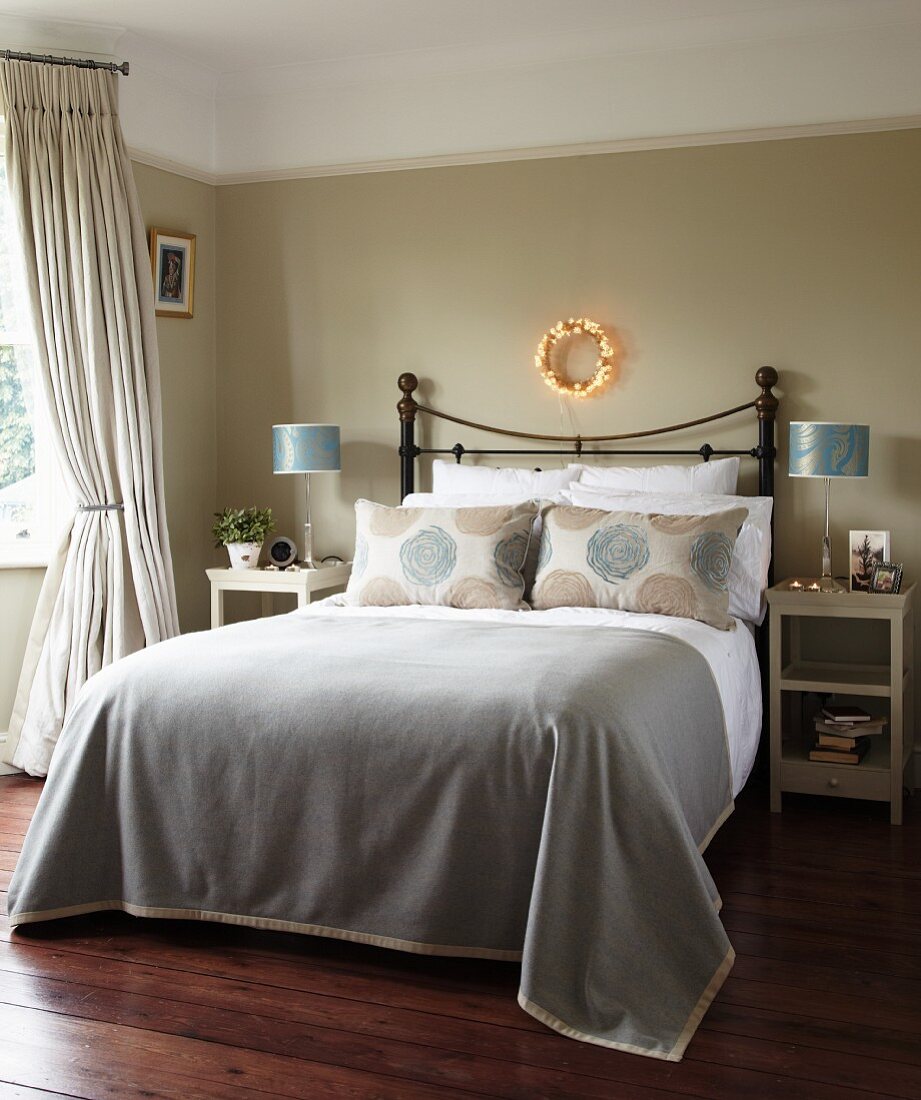 Elegantes Schlafzimmer mit traditionellem Flair, Doppelbett mit Metall-Kopfteil und grauer Tagesdecke vor getönter Wand mit Weihnachtsdeko