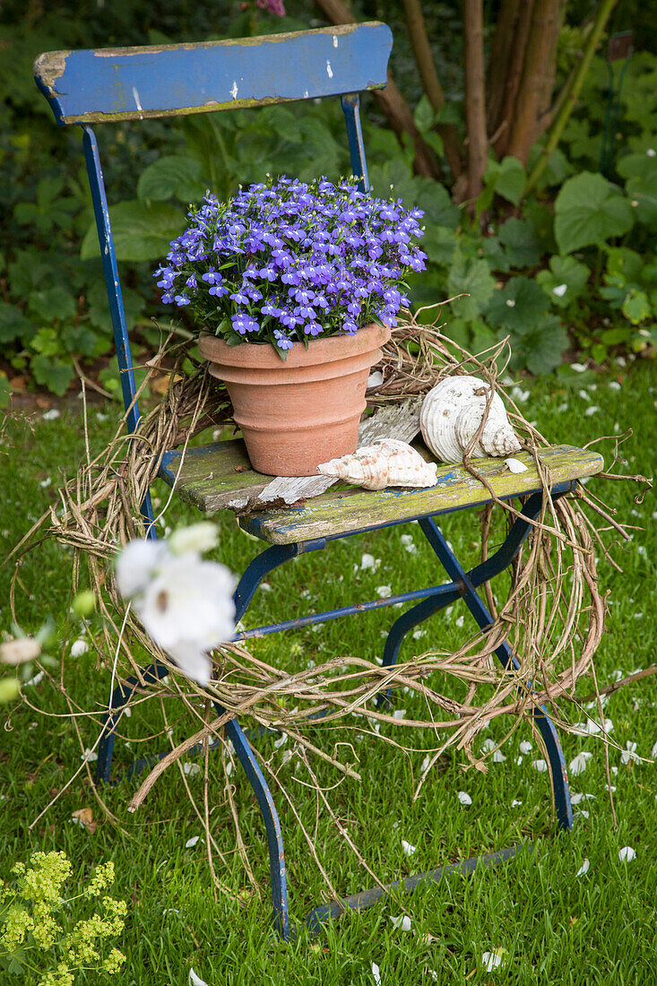 Alter Klappstuhl im Garten mit Blumen, Muscheln und Kranz