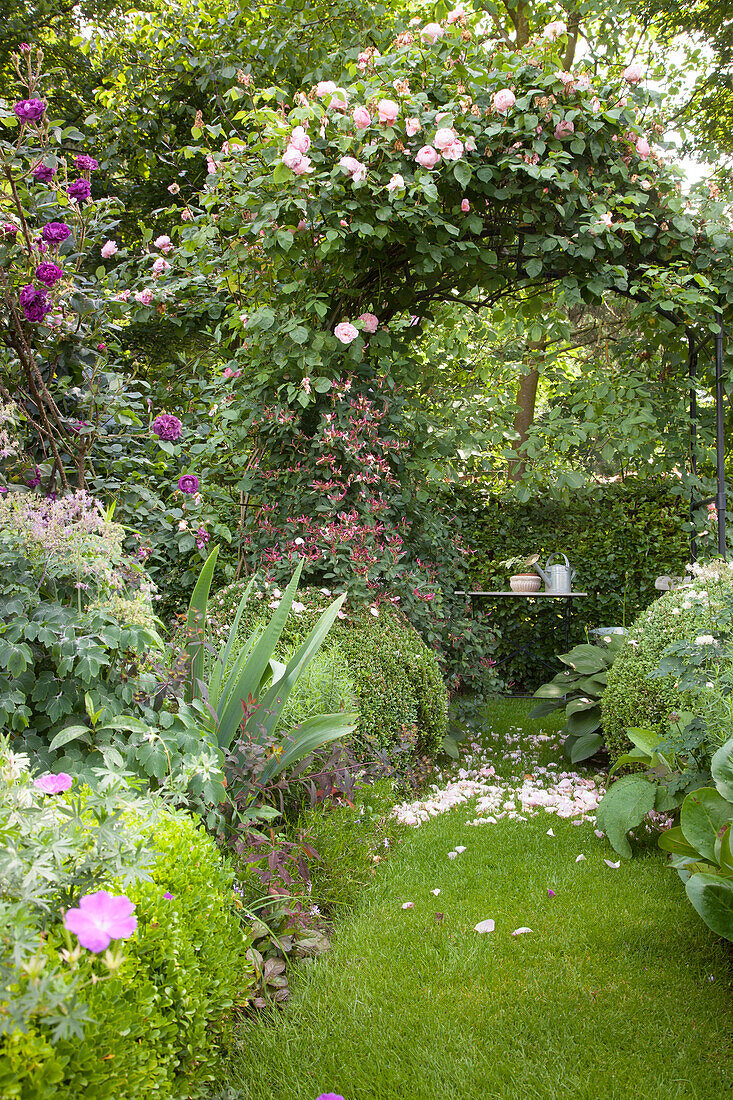 Rasenweg durch einen idyllischen Garten mit Rosenbogen