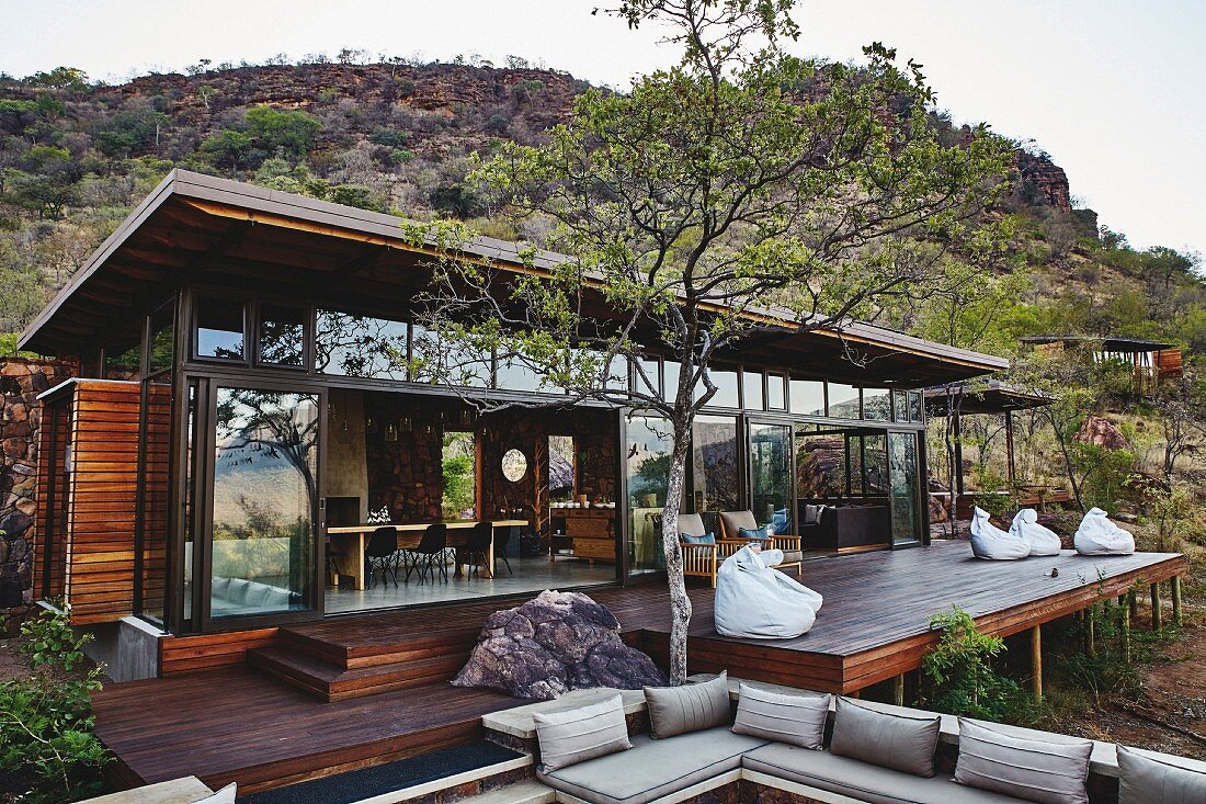 Moderne Safari-Lodge mit Glasfassade, grosszügiger Holzterrasse in naturbelassener Wildnis