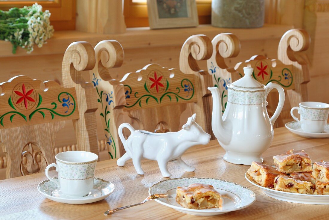 Coffee service and cake on wooden table and carved painted wooden chairs