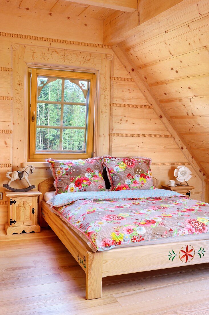 Doppelbett mit floral gemusterter Bettwäsche im Dachzimmer mit heller Holzauskleidung