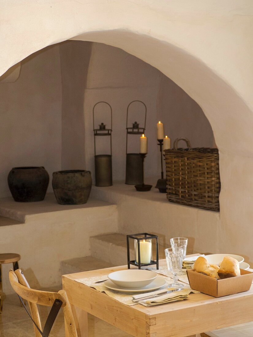 Small, simple dining area in front of arch with old, rustic vessels an candles on masonry steps and platforms