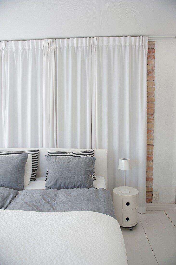 Schlafzimmer in Weiß, Doppelbett mit grauer Bettwäsche und bodenlangem Vorhang am Kopfende