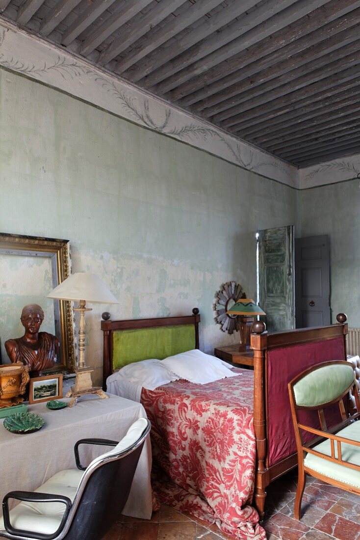 Schlafzimmer mit antikem Schlittenbett und gemustertem Plaid, daneben Tisch mit Retro-Drehsessel in mediterranem Ambiente