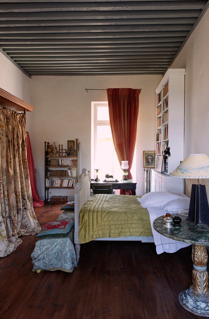 Antikes Schlittenbett mit Tagesdecke und Schrank mit gemustertem Vorhang in mediterranem Ambiente