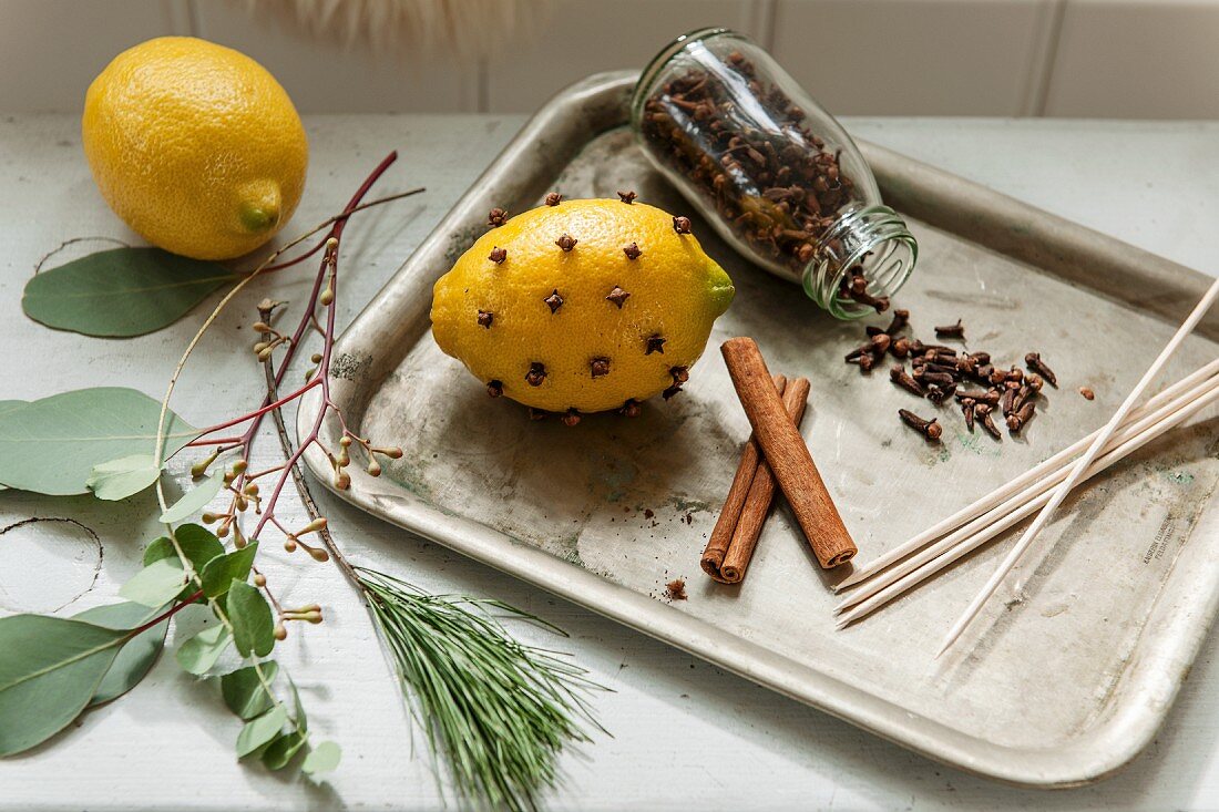 Mit Nelken gespickte Zitrone, offenes Glas mit Gewürznelken und Zimtstangen auf Vintage Tablett
