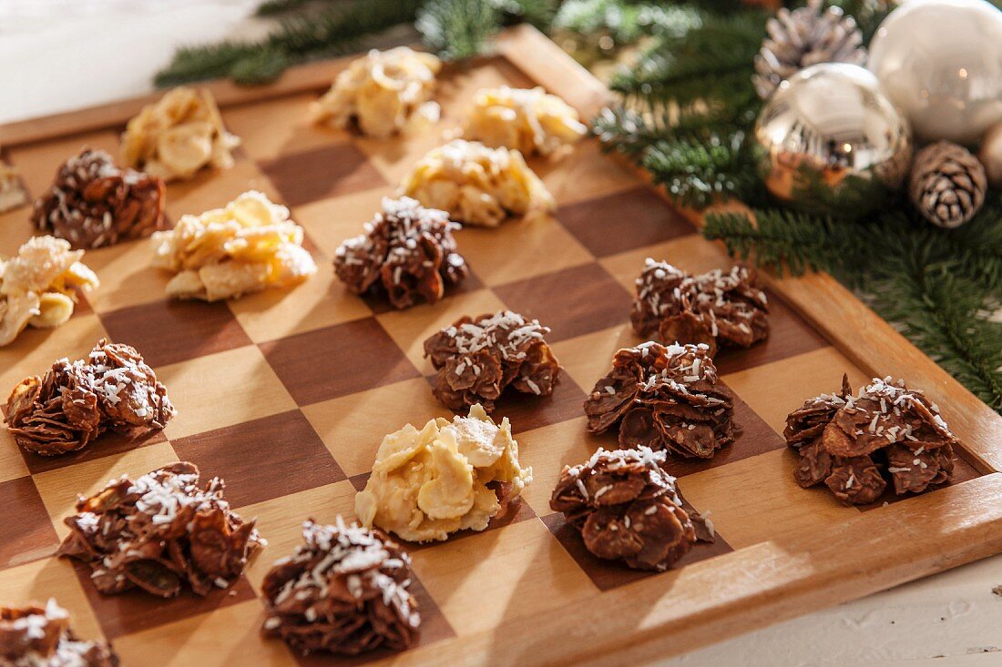 Light and dark cornflake cakes on chessboard next to Christmas decorations