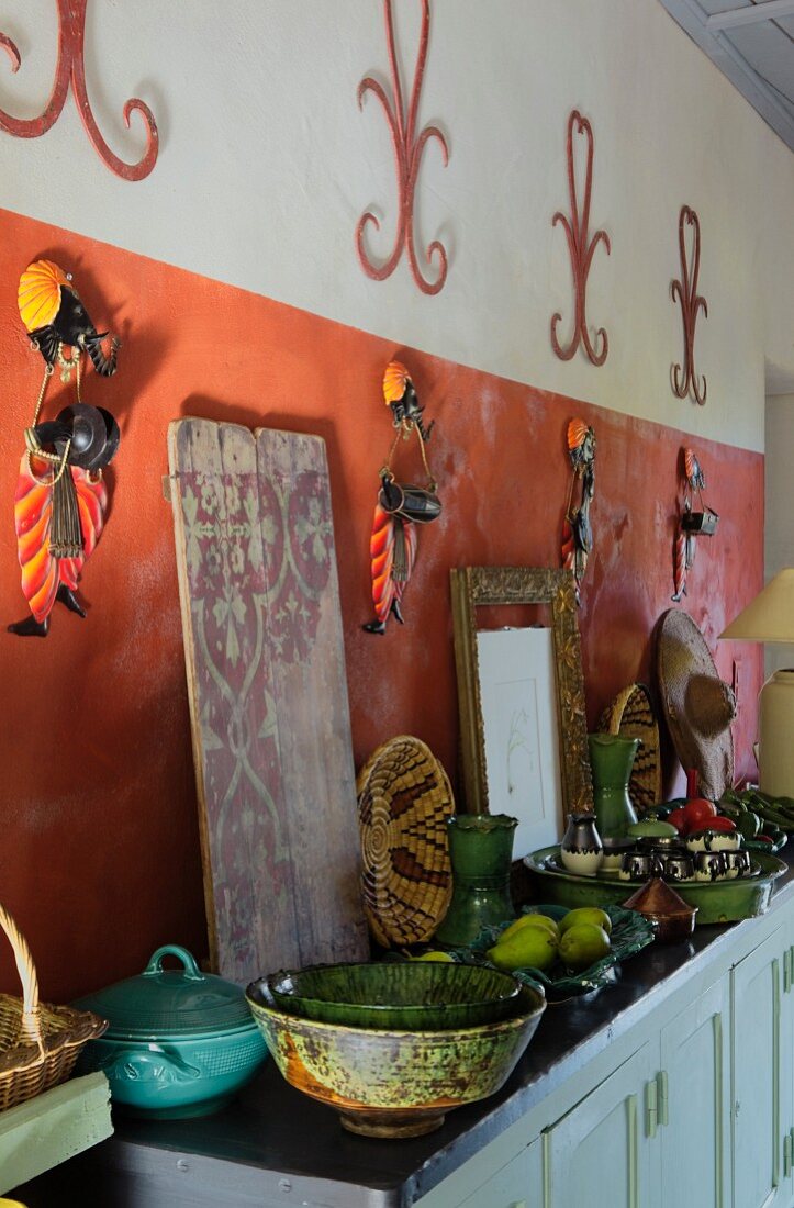 Grünes Keramikgeschirr mit Obst auf Sideboard vor rotbrauner Wand mit indischen Wanddekorationen