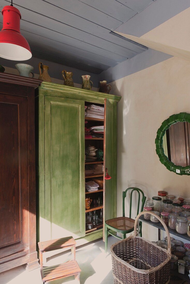 Basket in front of storage jars on table next to green-painted wooden cupboard with open door