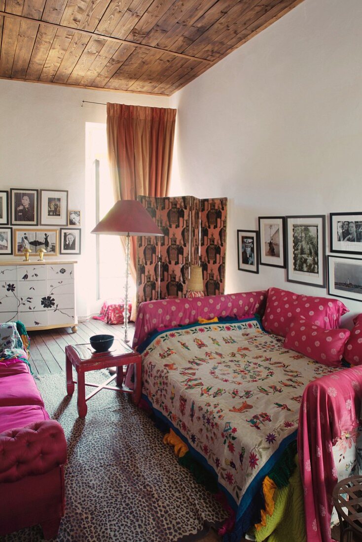 Gemütliches Bett mit folkloristischer Tagesdecke, Kissen in pinkfarbenen Bezügen in eklektischem Ambiente