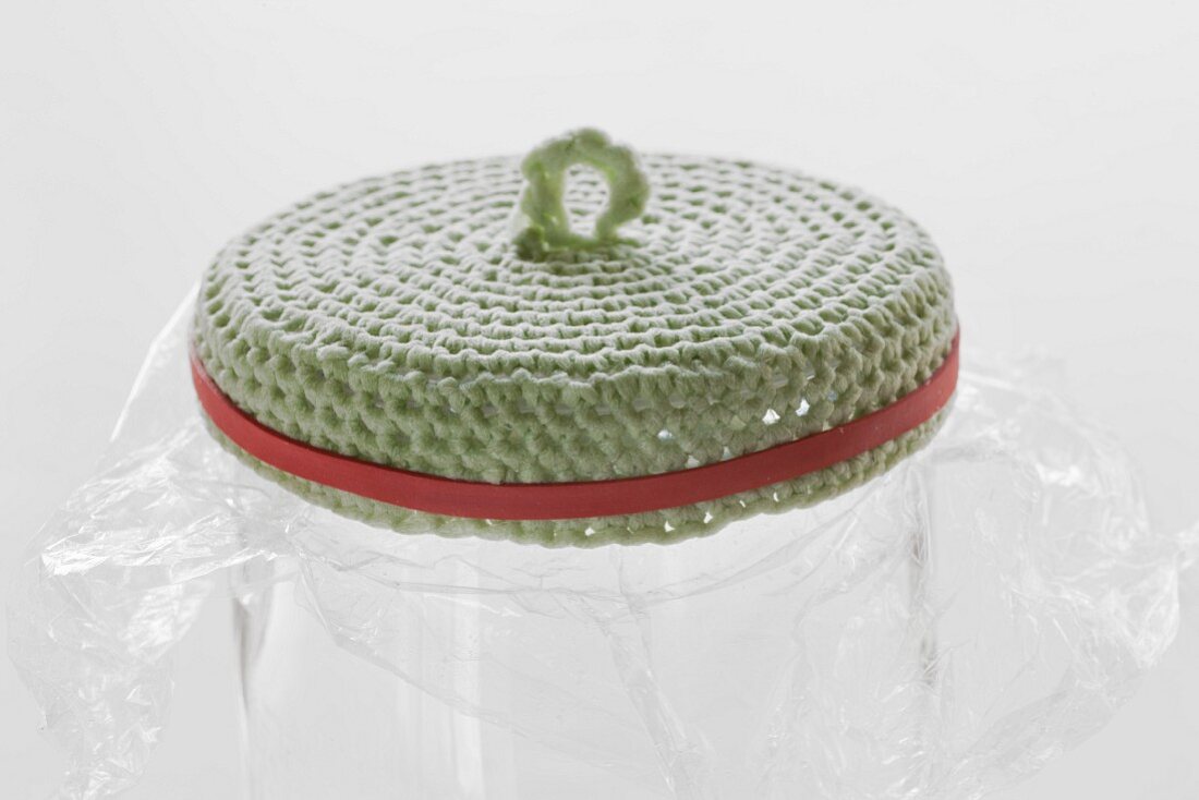Gehäkelter, eingekleisterter Deckel zur Formgebung mit Gummi auf Glasgefäß mit Frischhaltefolie gespannt