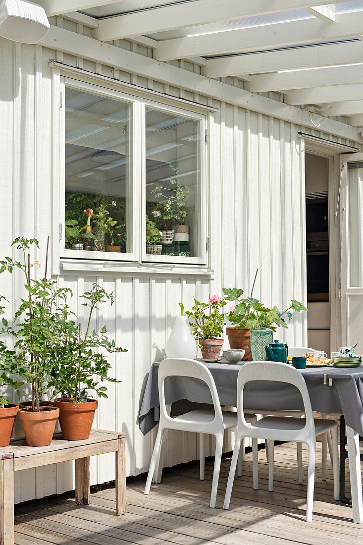 Terrasse mit weissen Kunststoffstühlen um gedeckten Tisch vor weißem Holzhaus