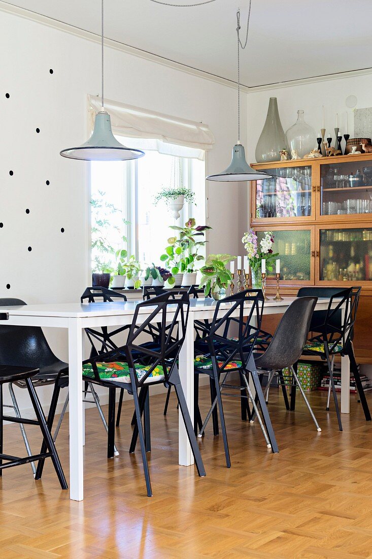 Schwarze Designerstühle um weißem Tisch und Pendelleuchten in Essbereich mit skandinavischem Flair