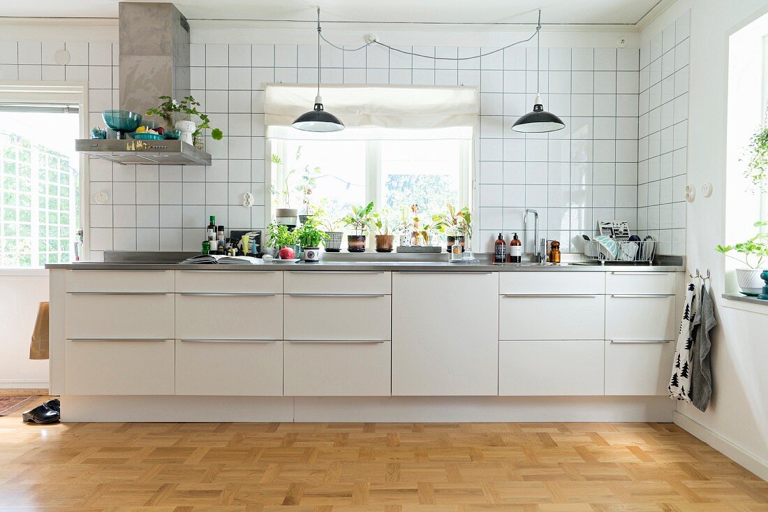 White kitchen counter with bar handles below window in tiled wall with house plants on windowsill
