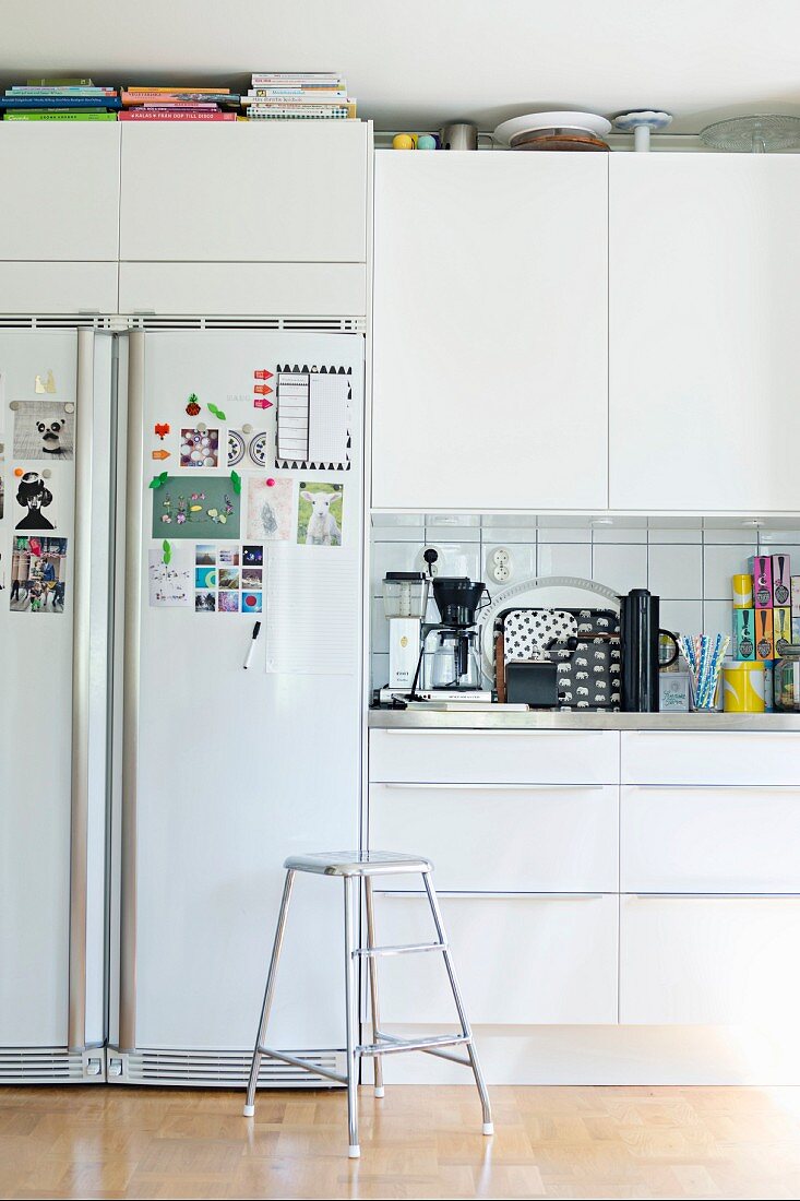 Filigraner Metallhocker vor weisser Einbauküche mit integrierter Kühlschrankkombination