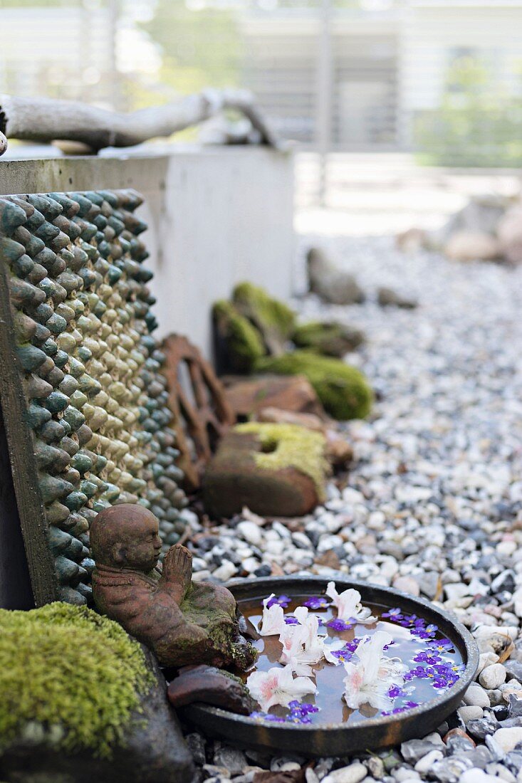 Praying figurine next to flowers floating in dish of water