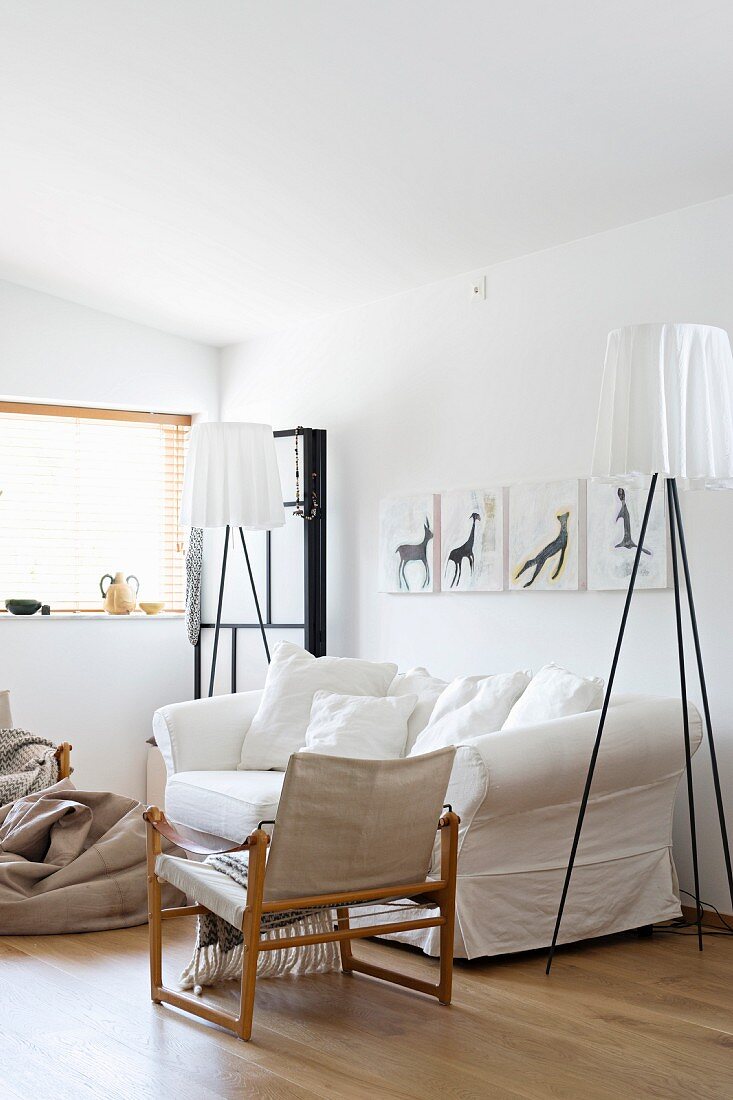Designer-Stehleuchten neben Hussen-Sofa, Sessel mit Holzgestell und Leinenstoff in weißem Wohnzimmer
