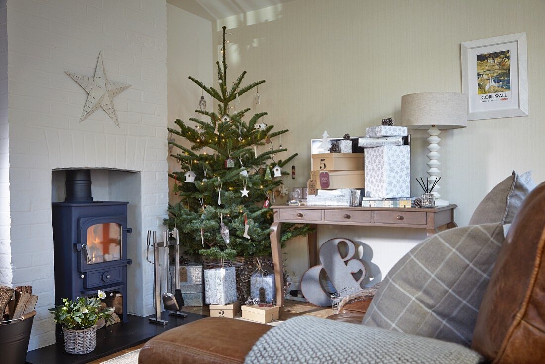 Ländliches Wohnzimmer mit geschmücktem Weihnachtsbaum neben Kaminofen und Konsolentisch mit Geschenken