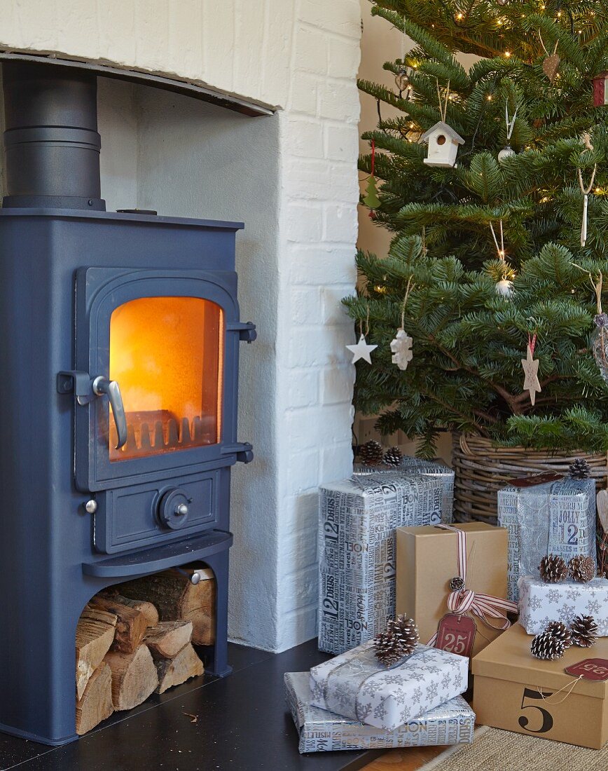 Gifts below Christmas tree next to cast iron log burner in fireplace