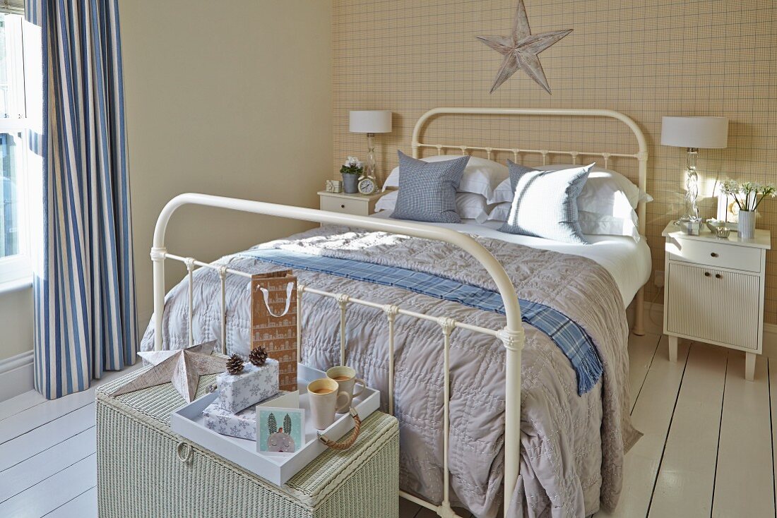Ländliches Schlafzimmer mit Doppelbett aus weißem Metall, auf Rattantruhe Tablett