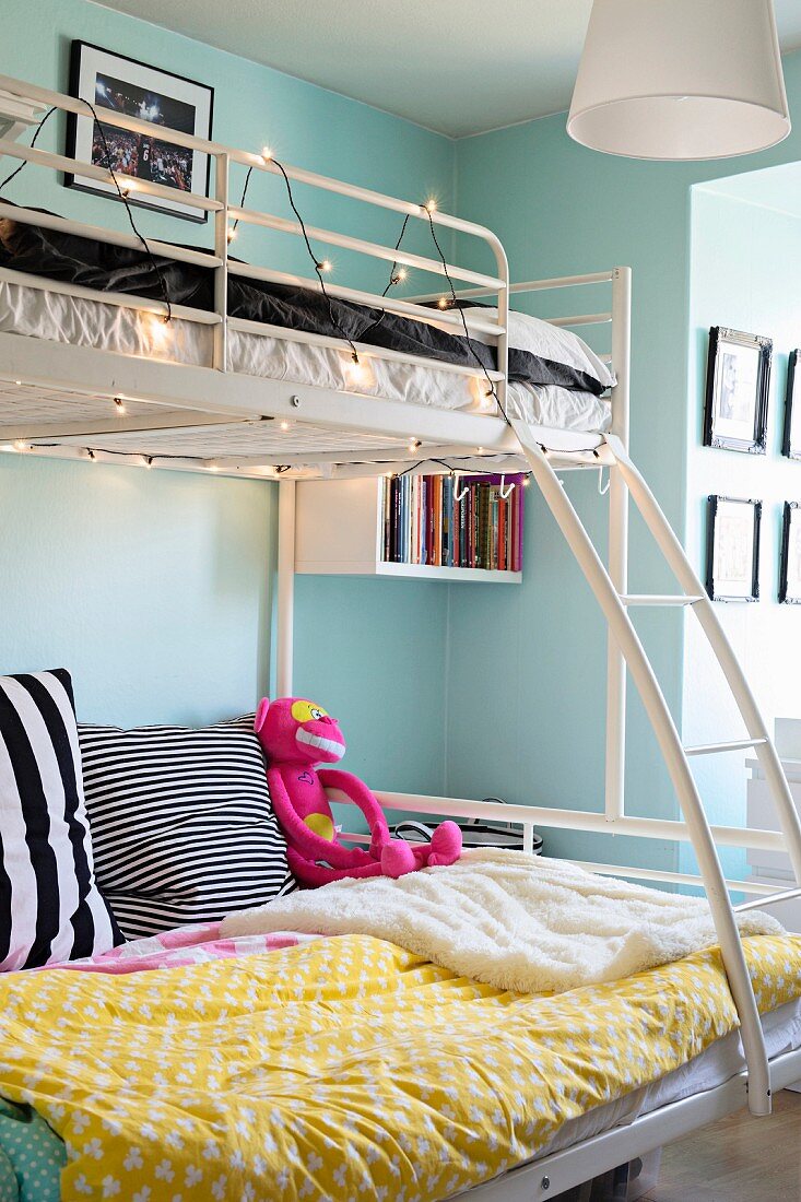 Weißes Metall-Stockbett mit Lichterkette und Leiter in Jugendzimmer mit hellblauer Wand