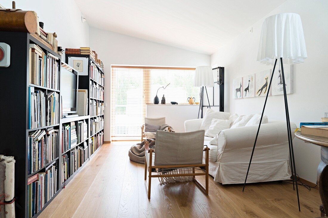 Designer-Stehleuchten neben weißem Hussensofa gegenüber Bücherwand mit Fernseher in Wohnzimmer