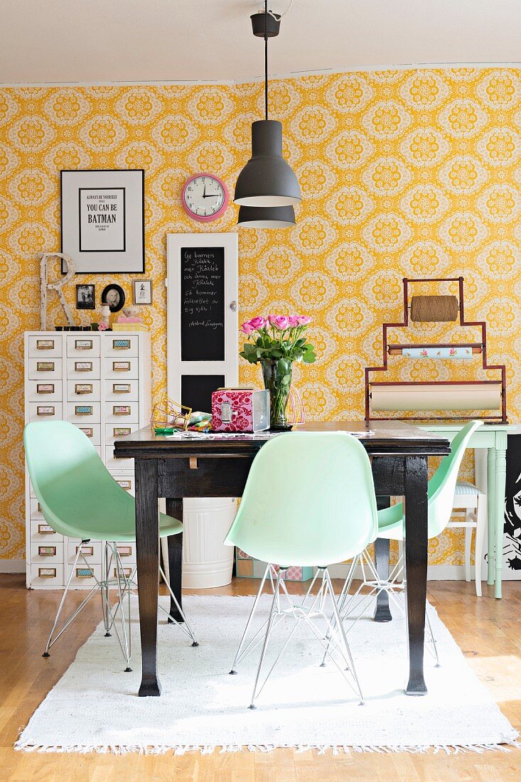 Pastel-green shell chairs around dark wooden table in dining room with yellow and white patterned wallpaper