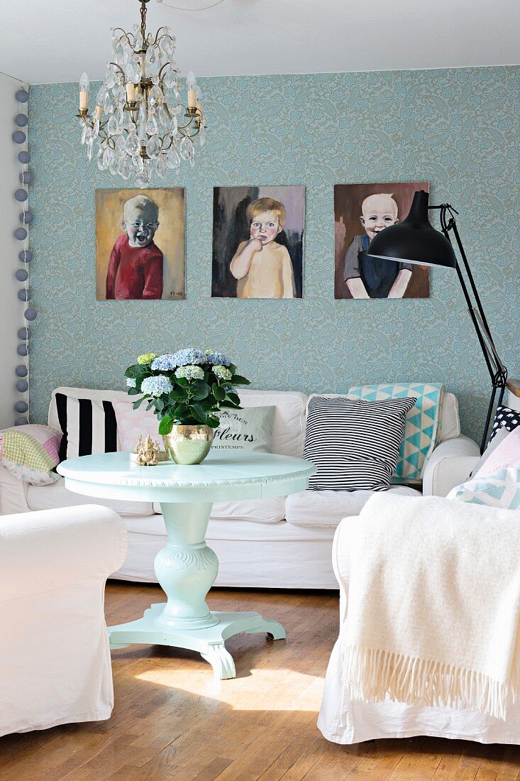 Runder Tisch, weiße Polstersessel und gemütliches Sofa vor tapezierter Wand mit Kinderportraits