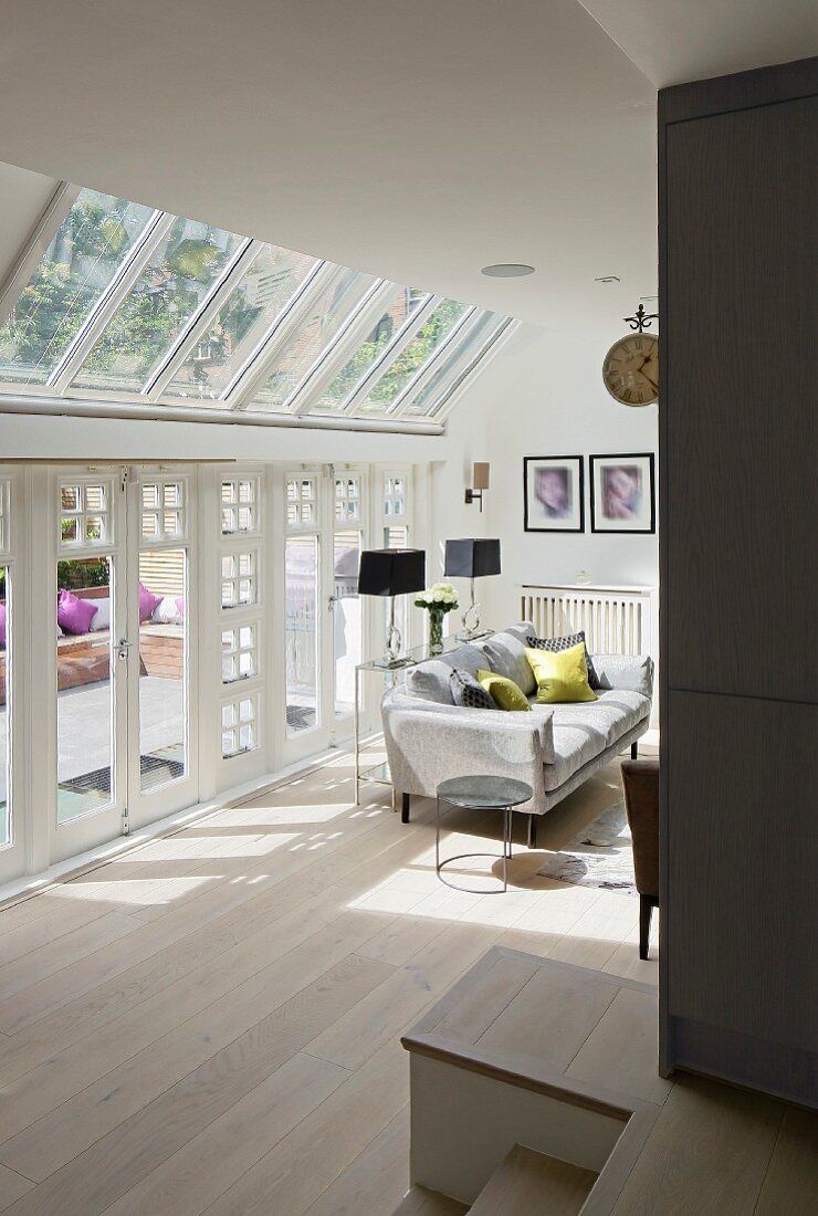 Blick auf sonnenbeschienenes Sofa vor Terrassenverglasung und Glasdach in elegantem Wohnambiente