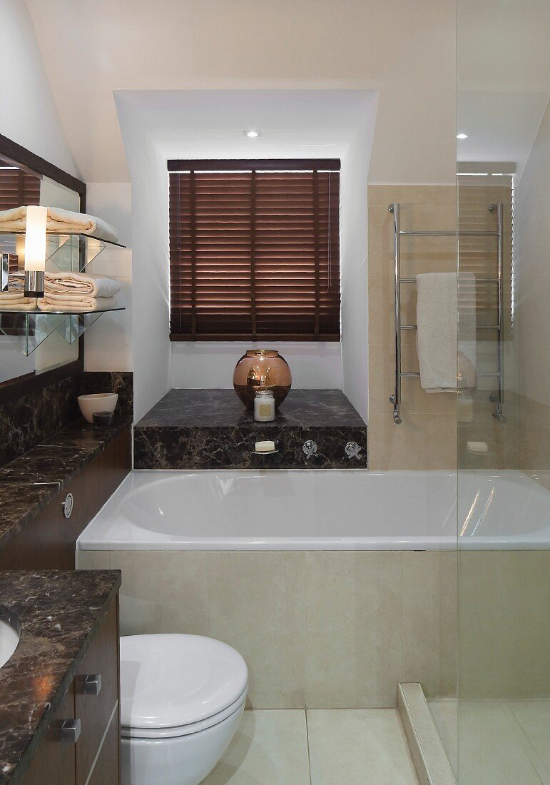 Dunkelfarbene Marmor-Waschtischplatte mit Ablageflächen, weiße Badewanne und Glas-Duschabtrennung im Bad
