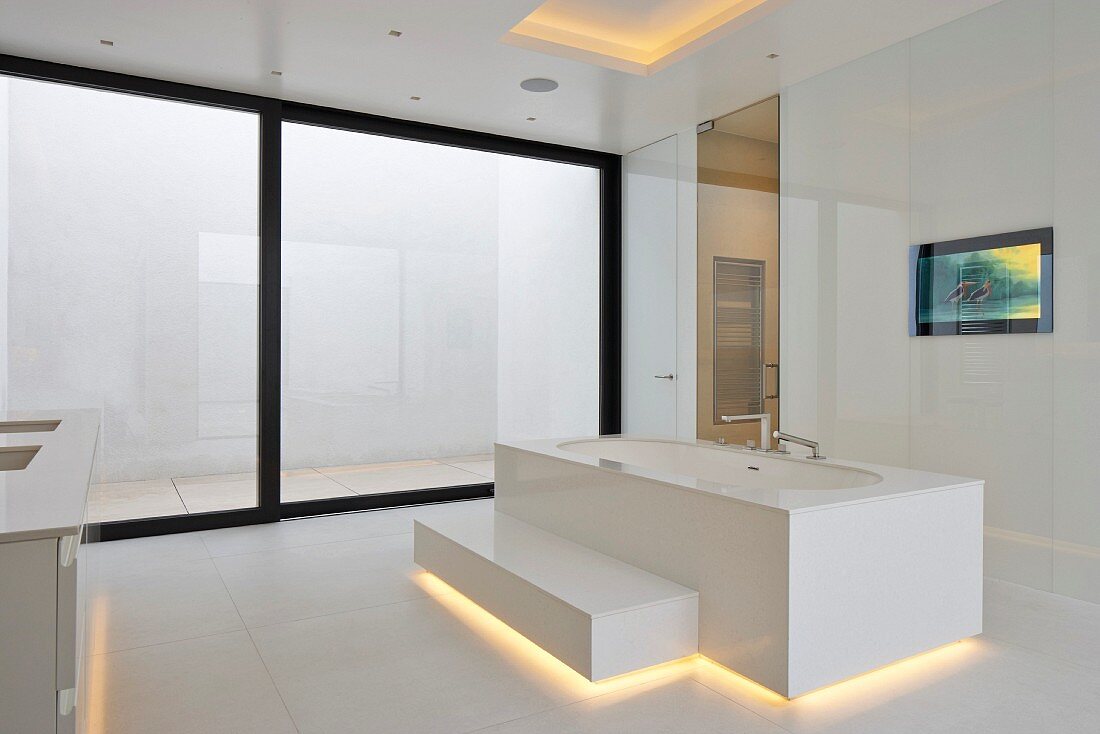 Designer bathtub with step and indirect lighting in minimalist, white, designer bathroom