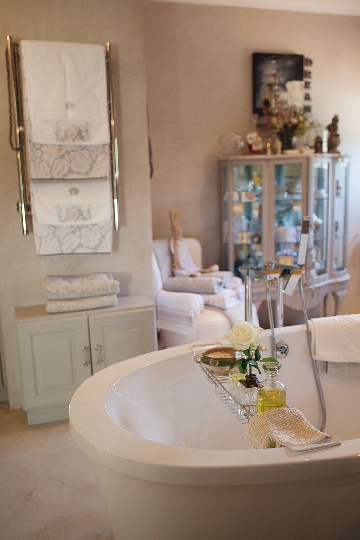 Free-standing bathtub with toiletries on bath caddy and towel rack above cabinet in background