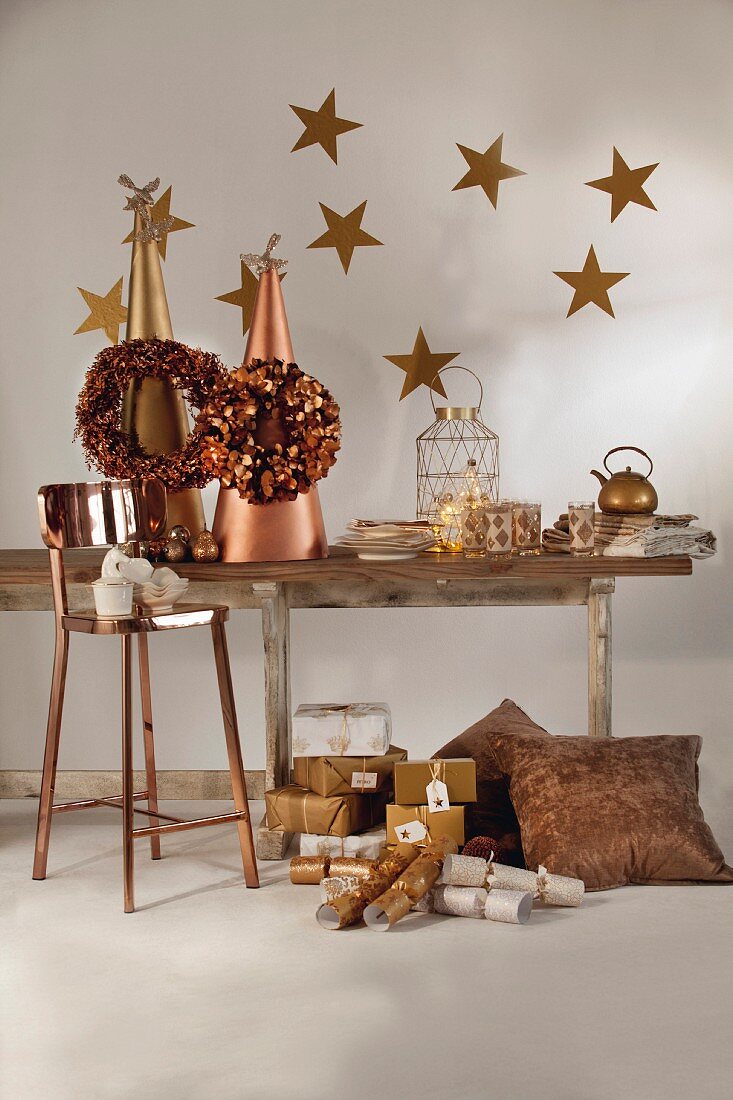 In Gold- und Bronzefarben weihnachtlich dekorierter rustikaler Holztisch mit Barhocker und drapierten Weihnachtsgeschenken am Boden
