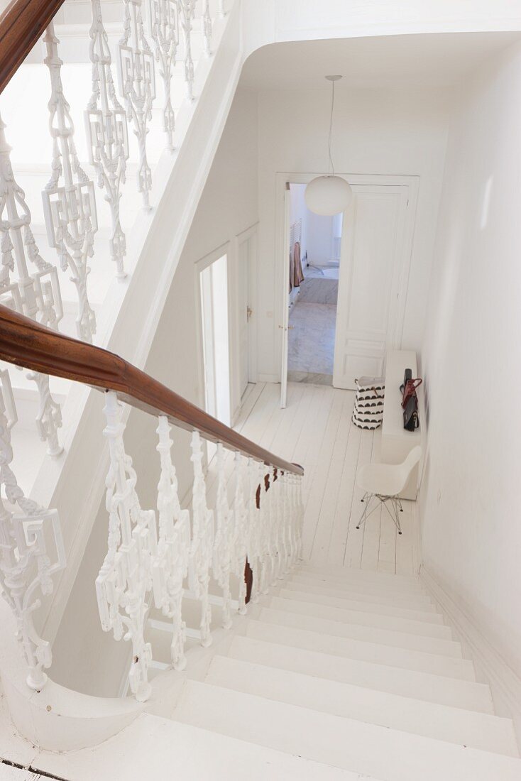 Treppenhaus mit weißem, Holzgeländer, Blick nach unten auf weiße Diele in Altbauwohnung