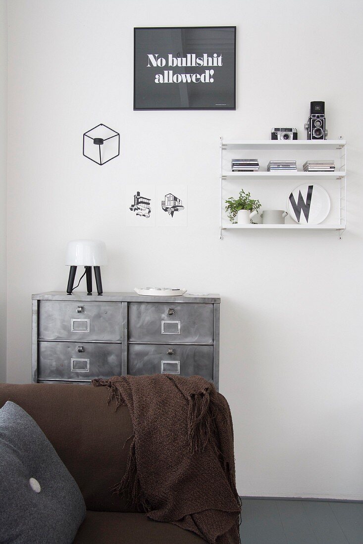 Braunes Sofa vor Metall- Schubladenschrank an weißer Wand mit String-Regal und Wanddeko