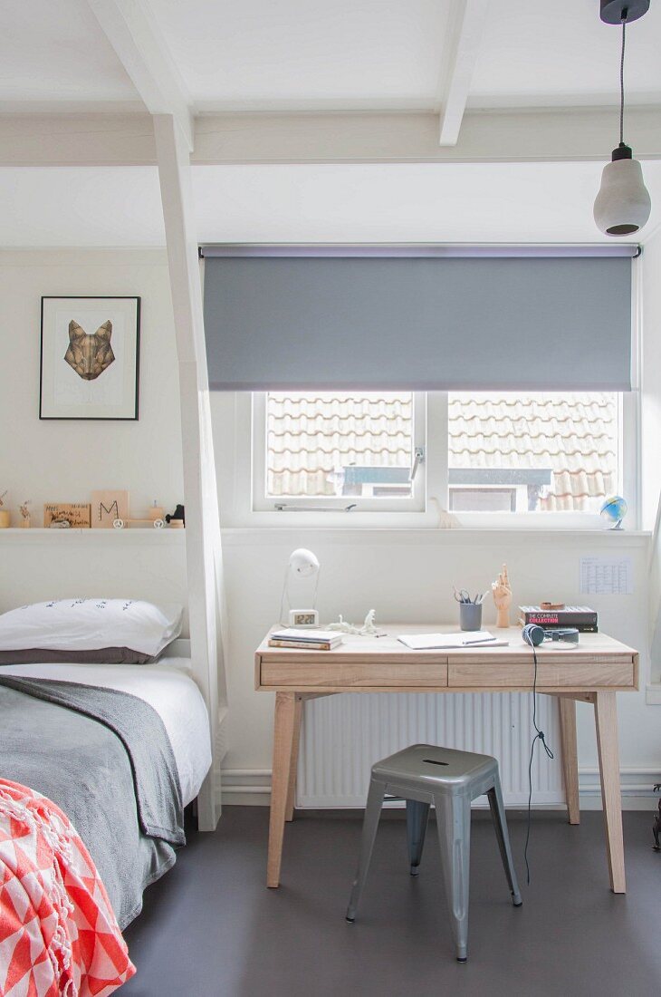 Holzschreibtisch und grauer Klassiker-Metallhocker vor Fenster mit Rollo in Jugendzimmer mit skandinavischem Flair
